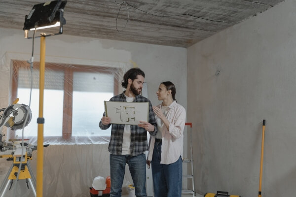 A couple plans their remodeling project inside a house that has plastic wrap on the walls mid-project.