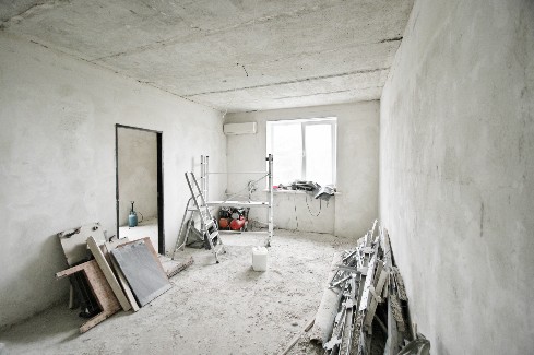 A room is bare and ready for remodeling with construction materials inside and a bright white light coming through the window reflected from snow.